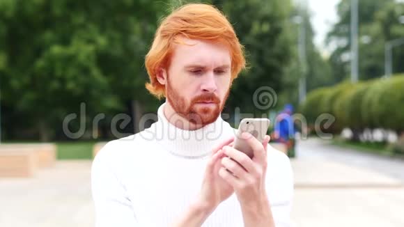 使用智能手机上网浏览有红头发的男人在户外视频的预览图