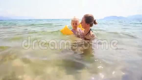 金发母亲挽着小女儿在蔚蓝的大海里视频的预览图