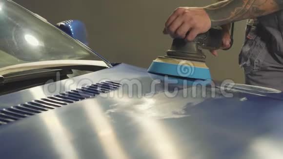 师傅在一个汽车车间里用抹油机打磨深蓝色跑车视频的预览图