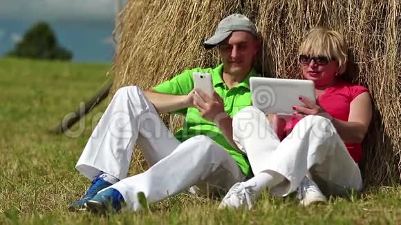 男人带着白色智能手机女人带着白色平板电脑坐在干草堆附近视频的预览图