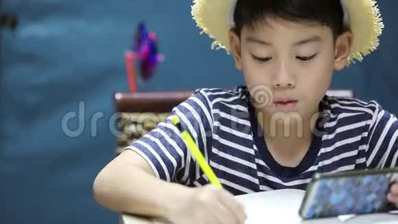 一个亚洲小男孩微笑着看着手机屏幕和绘画视频的预览图