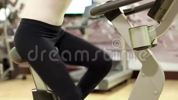 女人在健身房训练女人坐在运动自行车上转脚踏板视频的预览图