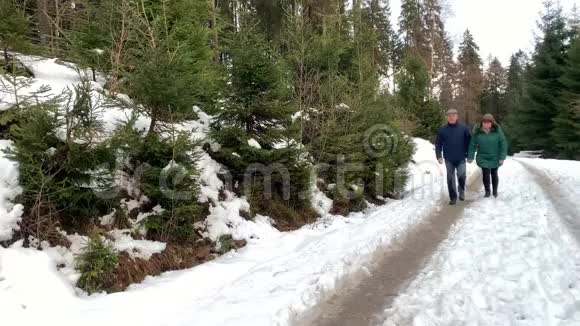 穿着夹克的女人和男人在冬天穿过一片雪林视频的预览图