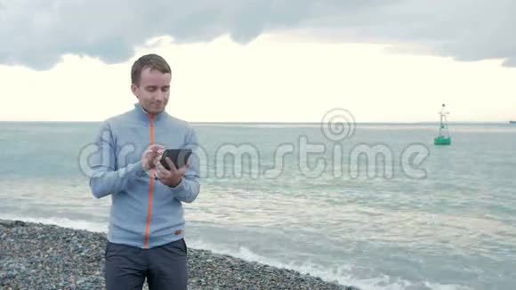 一个人拿着石碑沿着海边散步他检查社交网络上的信息并浏览照片视频的预览图