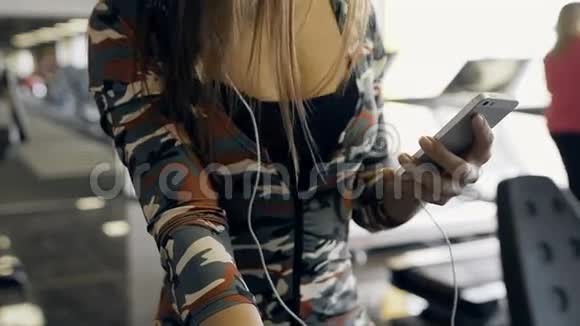 年轻的运动女性在健身房里骑着一辆固定的自行车用耳机听音乐视频的预览图
