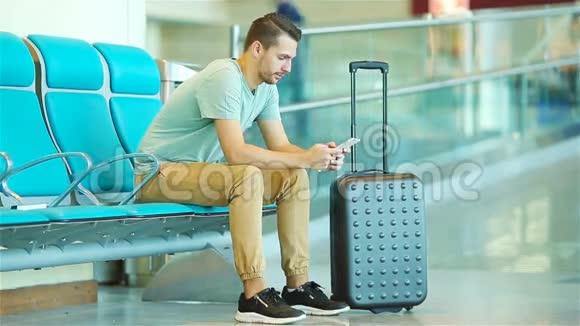 在机场休息室等飞机的年轻人带智能手机的白人男子在候诊室视频的预览图