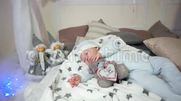 可爱的小男孩孩子睡觉时抱着玩具小孩子睡觉婴儿躺在床上躺在滑块和帽子里视频的预览图