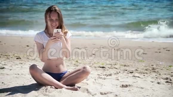 女孩带着手机坐在沙滩上靠近大海和蓝天初恋视频的预览图