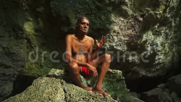 穿短裤的成年男性坐在洞穴深处的岩石上视频的预览图