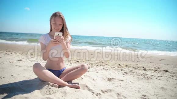 女孩带着手机坐在沙滩上靠近大海和蓝天初恋视频的预览图