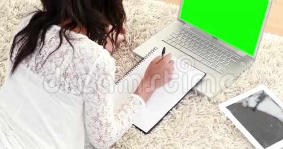 微笑的女人躺在地板上用笔记本做作业视频的预览图