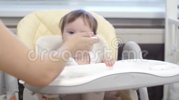 孩子坐在厨房的高椅上吃汤匙煮的粥视频的预览图