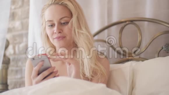 年轻的女人躺在床上拿着手机女孩上网和别人聊天视频的预览图