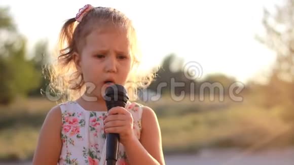 童女在夏日夕阳的余晖中对着麦克风唱着一首歌视频的预览图
