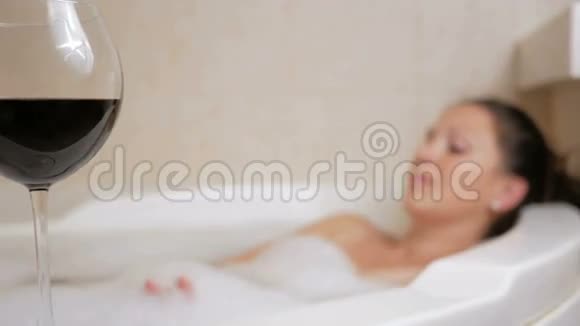 漂亮的女孩用一杯酒泡澡一个大大的白色澡盆脸上洋溢着喜悦松弛概念视频的预览图
