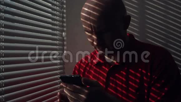 一个带智能手机的人站在窗户边带百叶窗视频的预览图