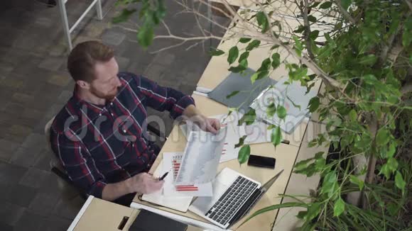 留胡子的人坐在环境办公室里看着纸上的数字视频的预览图