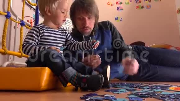爸爸和他可爱的金发小儿子一起组装拼图父亲和他的小男孩在家有空闲时间4K视频的预览图