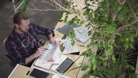 留胡子的人坐在环境办公室里看着纸上的数字视频的预览图