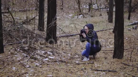 一个女孩带着相机拍摄大自然的照片这是一片秋天森林里的风景慢动作电影镜头视频的预览图