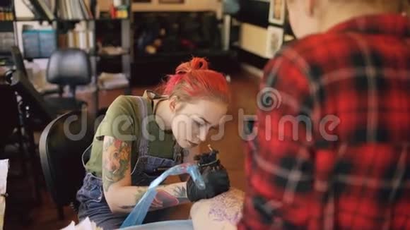 年轻的女红发纹身艺术家纹身图片在客户腿上素描在工作室室内视频的预览图
