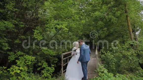 美丽的新娘和新郎在森林里的一座古老的铁桥上新郎爱抚他的爱人视频的预览图