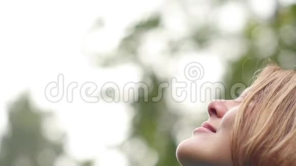 一个年轻的女人呼吸着干净的空气微笑着看着天空愉快地闭上眼睛视频的预览图