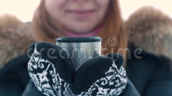 年轻可爱的女人在冬天的时候拿着一个热水瓶里的热茶杯子视频的预览图