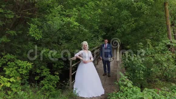 美丽的新娘和新郎在森林里的一座古老的铁桥上新郎爱抚他的爱人视频的预览图