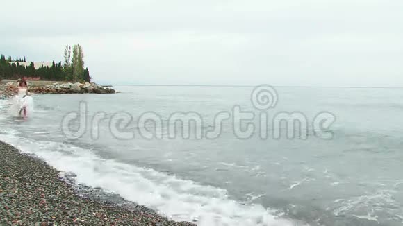 穿着白衣服沿着海滩奔跑的年轻女子视频的预览图