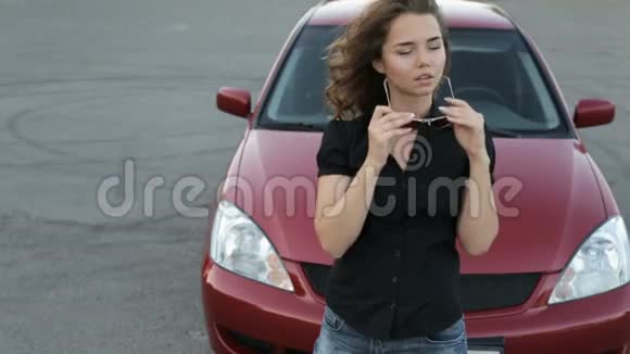 戴墨镜的女孩在红车背景下摆姿势视频的预览图