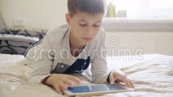 年轻的十几岁的男孩在床上看数字平板电脑视频的预览图