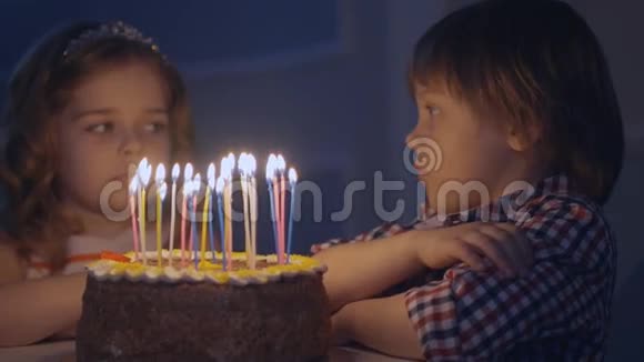 一个小男孩和一个女孩在庆祝蛋糕上看蜡烛并许愿视频的预览图