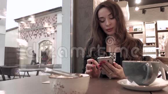 漂亮的黑发女孩在咖啡馆里用手机4K视频视频的预览图