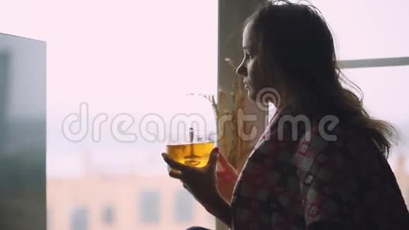 坐在窗台上喝着茶在窗外沉思坐在格子里的病态悲伤的女人1920x1080视频的预览图
