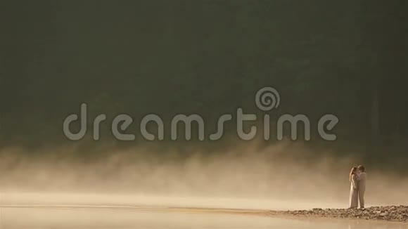 在风景如画的山湖上一对身穿乌克兰民族服装的幸福乡村夫妇在夕阳下金色的薄雾中接吻视频的预览图