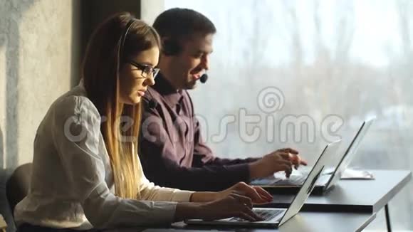 侧观美丽的年轻商务女性和英俊的商人在耳机使用笔记本电脑时在办公室工作视频的预览图