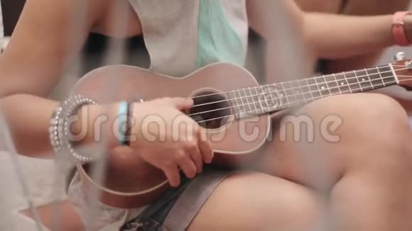 穿短裤的坐着女孩在街上调棕色的四弦琴吉他夏日阳光明媚音乐字符串声音视频的预览图