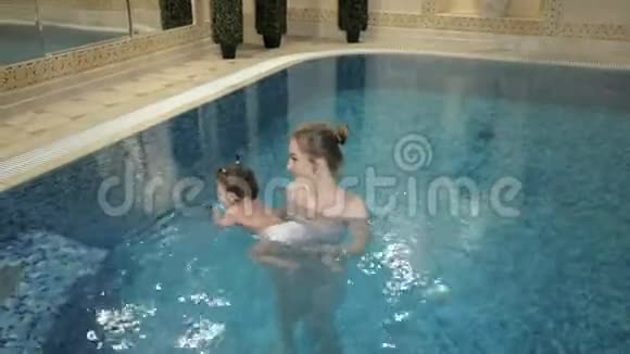 健康的家庭妈妈教女婴在游泳池游泳视频的预览图