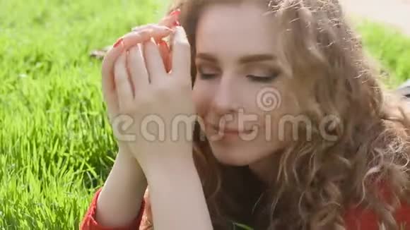 幸福微笑的女人躺在绿草上享受生活年轻的女人在春天公园户外玩得很开心视频的预览图
