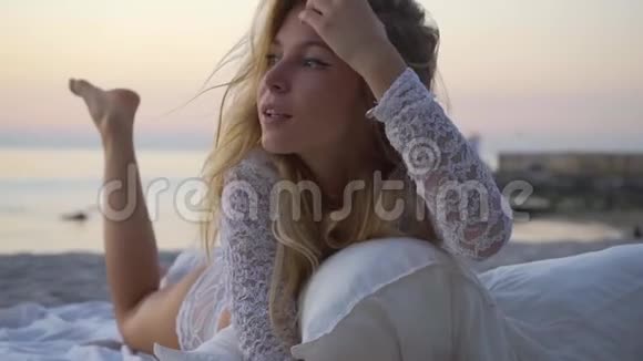 那个女孩躺在沙滩上枕头和毯子之间日落浪漫慢动作特写美丽的视频的预览图