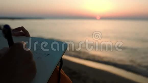 日落时分坐在海边做笔记的女人视频的预览图