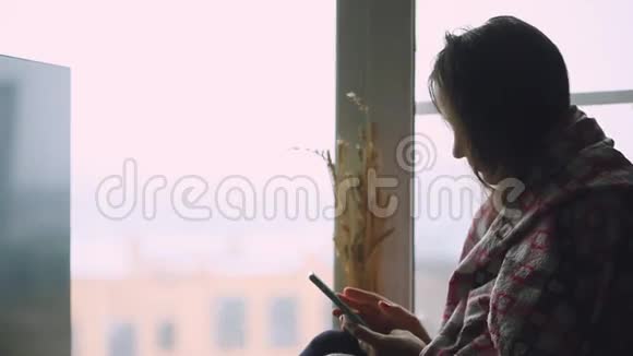 伤心体贴的女人坐在窗台上一边用手机看着窗户1920x1080视频的预览图
