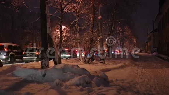 白雪覆盖的街道有美丽的树木和雪堆在路灯的灯光下通过车辆视频的预览图