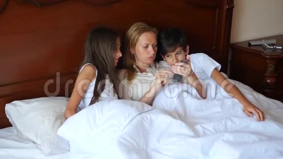 一个幸福的家庭躺在床上看着他们的智能手机上的东西4K慢动作视频的预览图