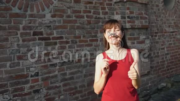 年轻的女人拿着胡子在棍子上站在砖墙旁边视频的预览图