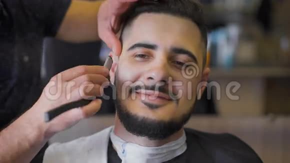 沙龙里的嬉皮士发型专业理发师使用直剃须刀制作胡须趋势形态视频的预览图