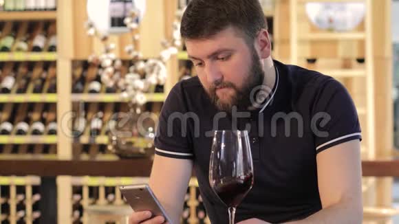 一个年轻人在喝红酒时使用智能手机一个孤独的男人拿着一杯红酒一个穿着一件衣服的年轻人视频的预览图