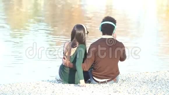 一对情侣坐在湖边用耳机听音乐视频的预览图