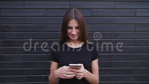 一位漂亮的年轻女士戴着眼镜用手机对着砖墙背景特写镜头视频的预览图